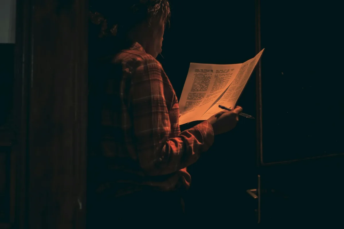 A man reading documents by warm candlelight in a dark, quiet room