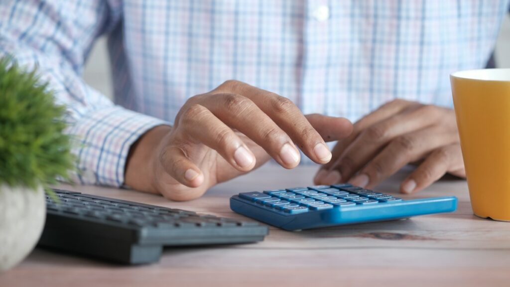 Hand using a calculator while comparing retirement benefits