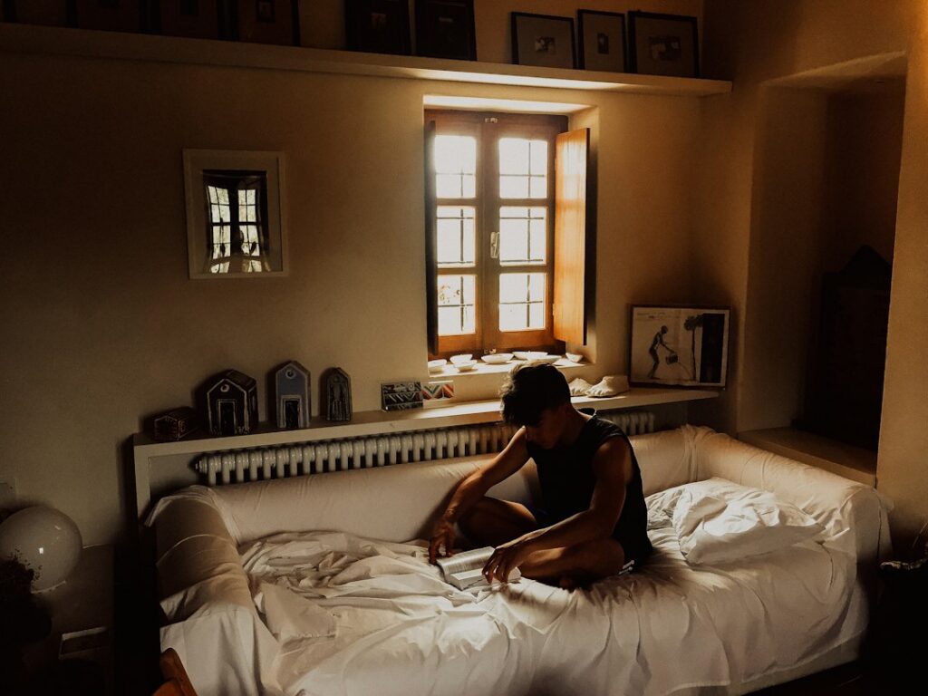 Tired man sitting on the edge of a bed in morning light