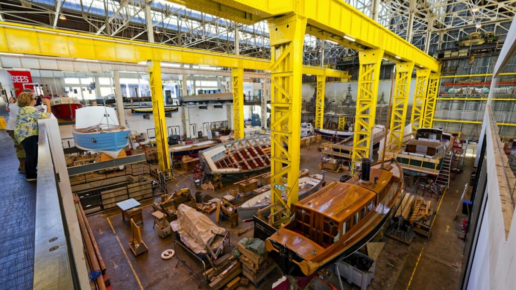 People looking at wooden boats under construction in a workshop
