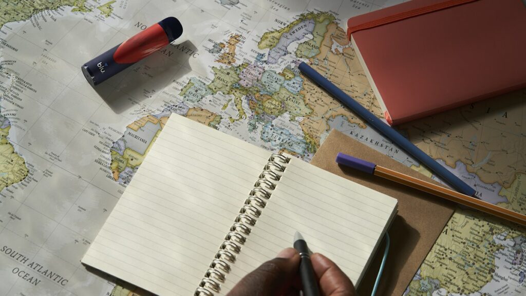 Person writing in a notebook beside a world map