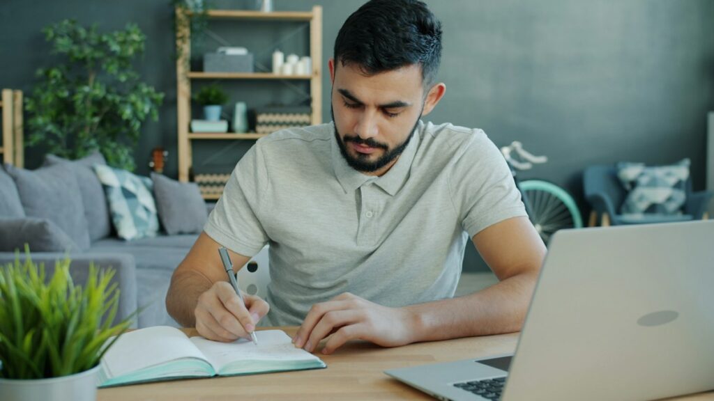 Man taking notes at a desk while reviewing financial goals