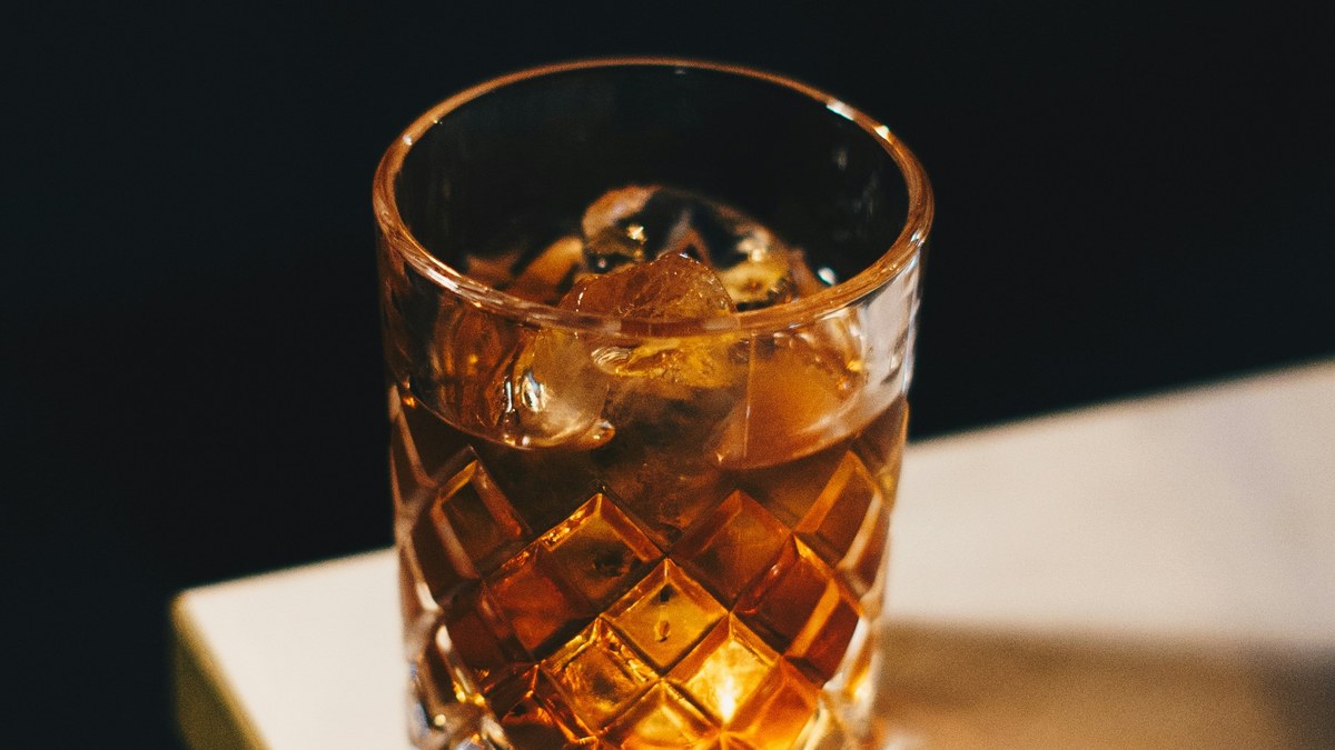 Glass of amber liquor with ice on a tabletop