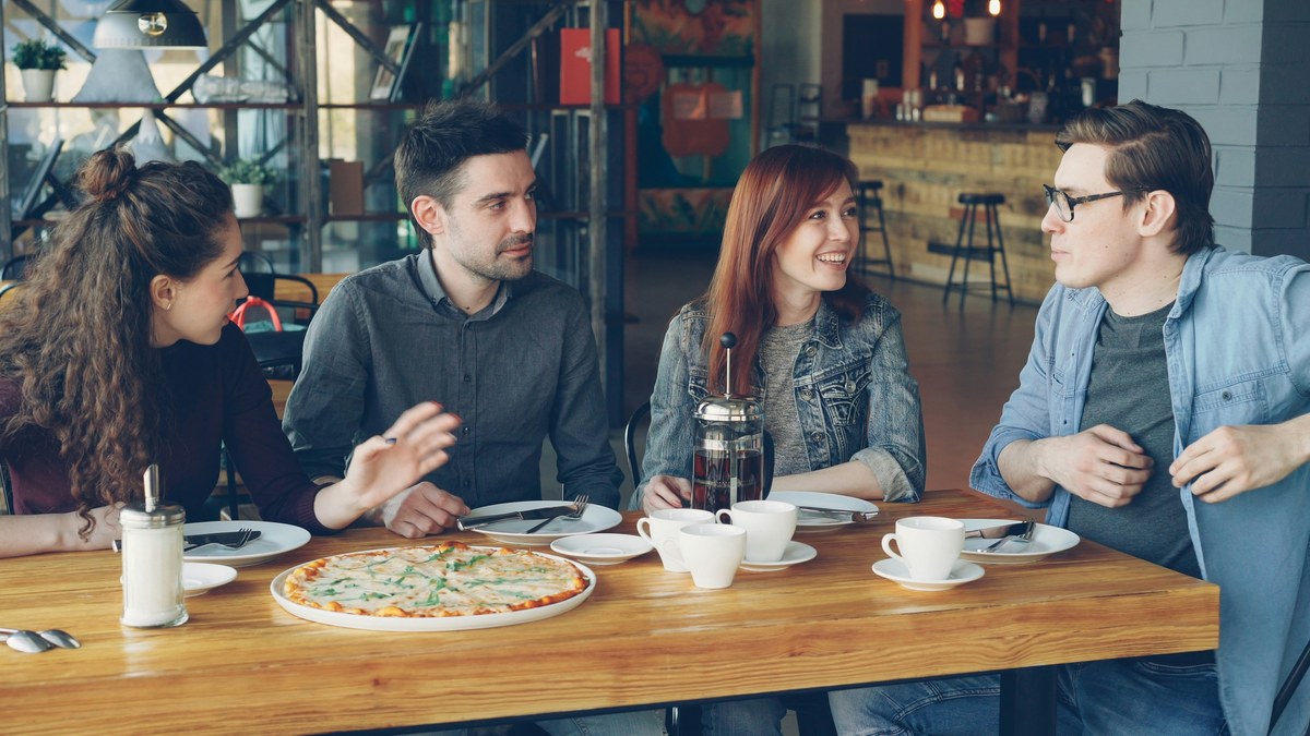 Four people talking over coffee and food at a cafe table