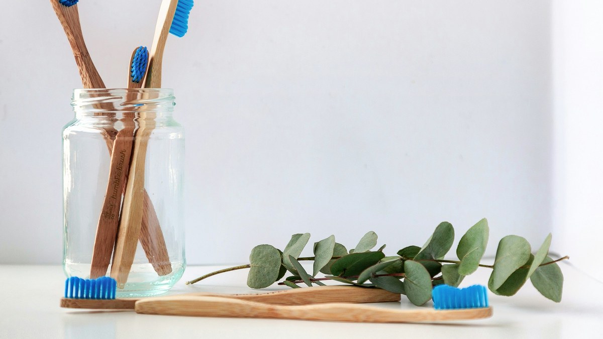 Bamboo toothbrushes standing in a glass beside greenery