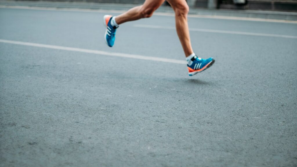 Runner's legs and shoes in motion on a paved road