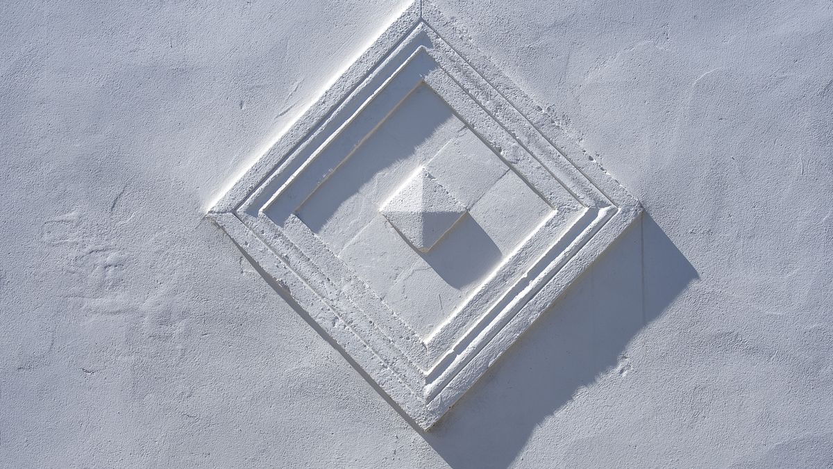 Close-up of a white textured wall with subtle raised geometric forms and shadows