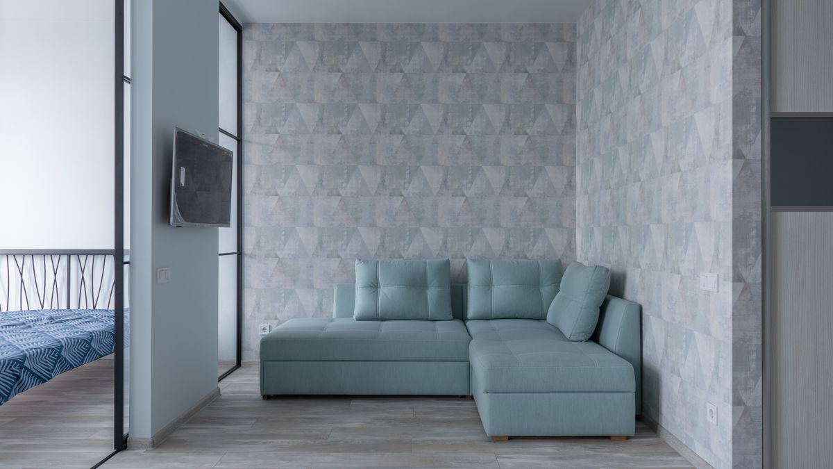A contemporary living room uses a geometric wallpaper feature behind an aqua sofa