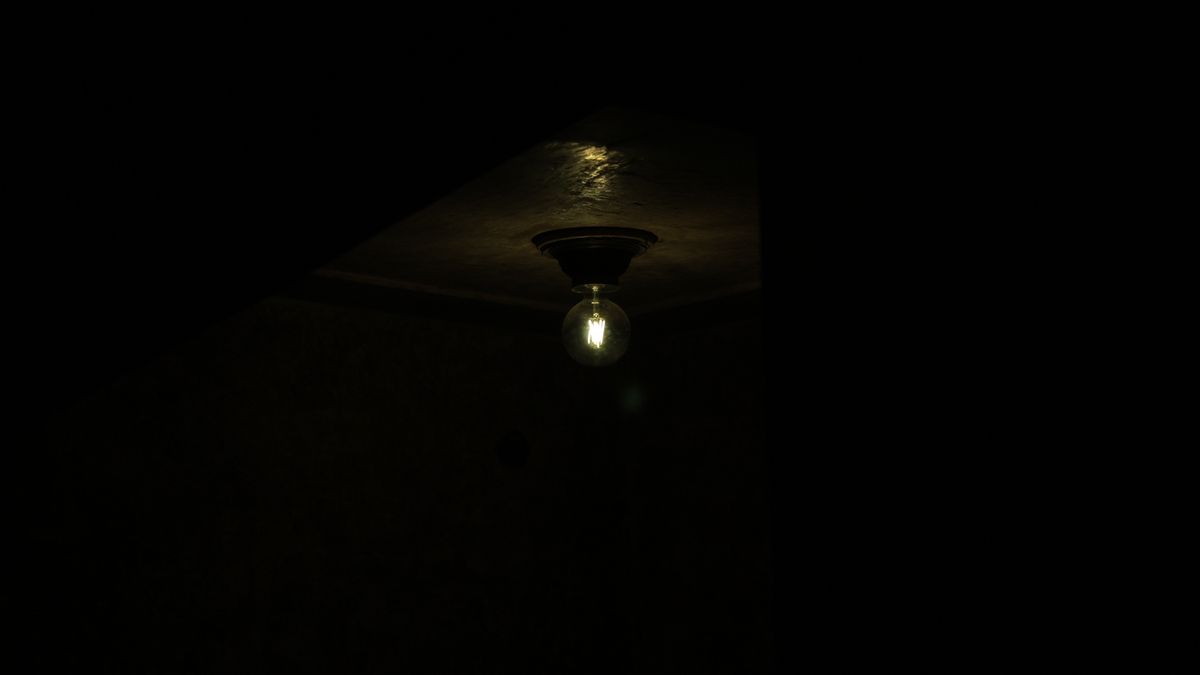 Dark ceiling and wall surrounding a single illuminated hanging bulb