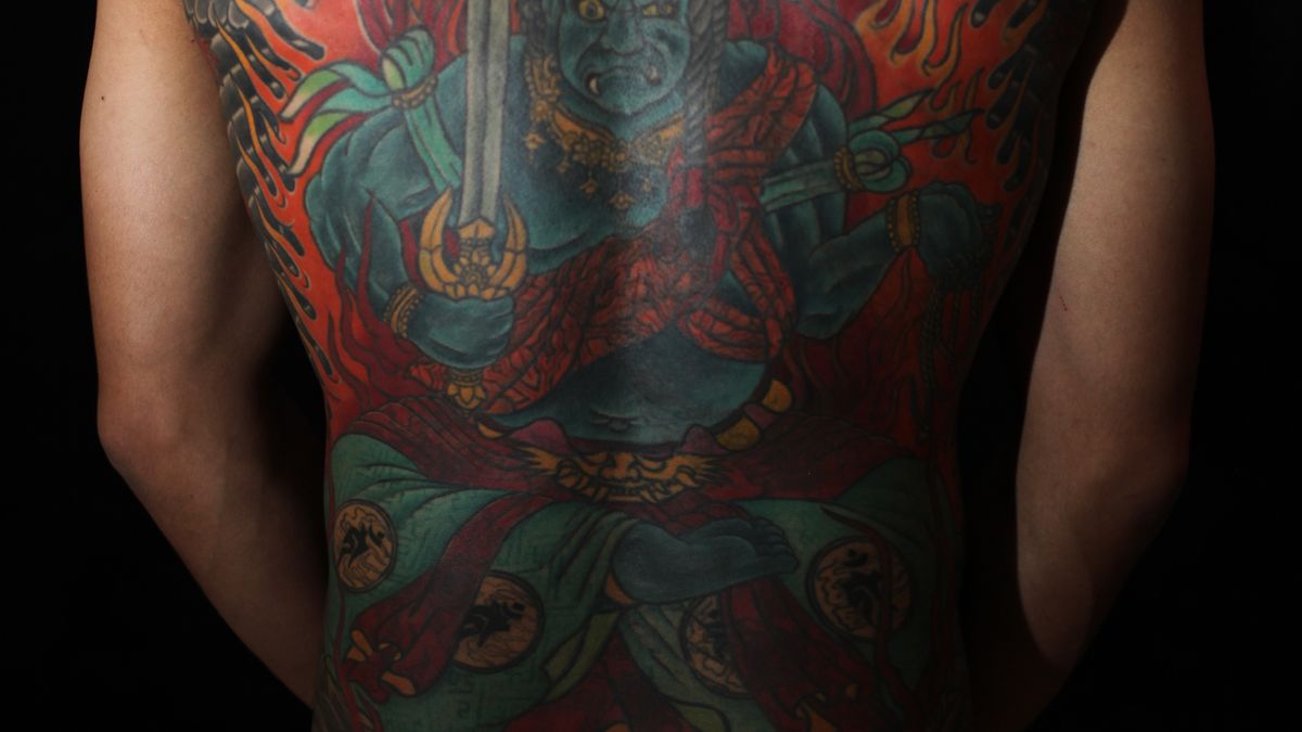 A tattooed mythological warrior figure with a sword and layered color across a man's back