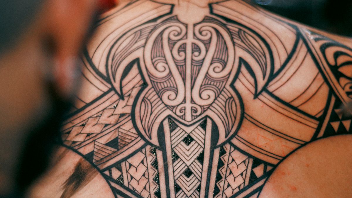 A large dark ornamental tattoo on a person's back shows detailed blackwork and patterned forms