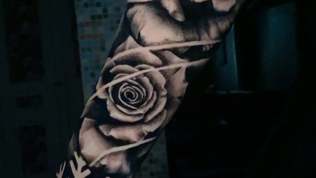 Close-up of a large black and grey rose composition tattooed along a forearm, with shaded petals and connecting lines
