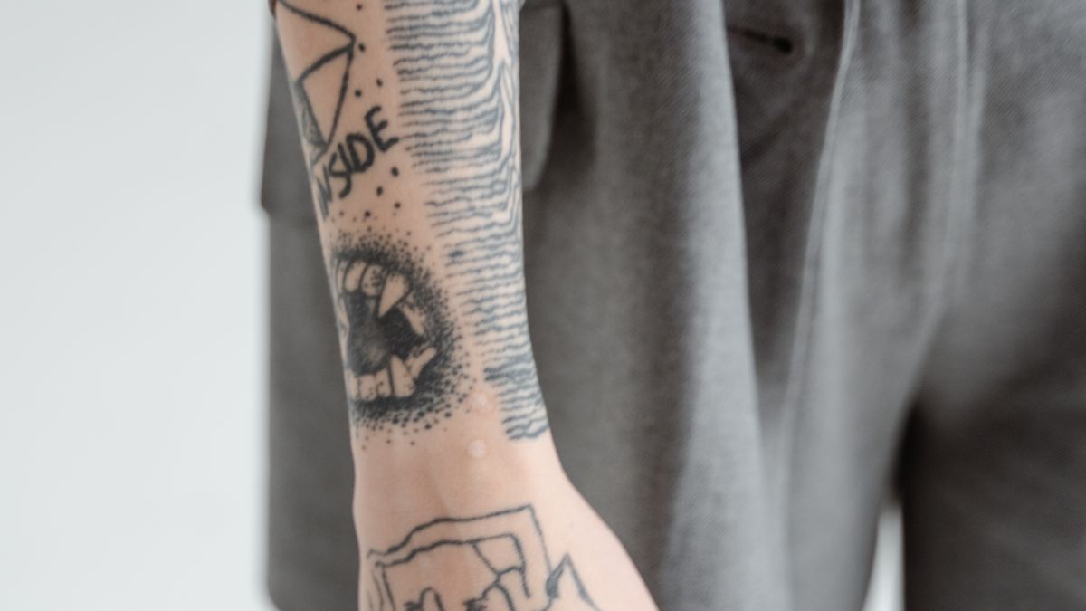 Forearm bearing several different black linework tattoos including an eye design and geometric patterns with visible gaps between motifs