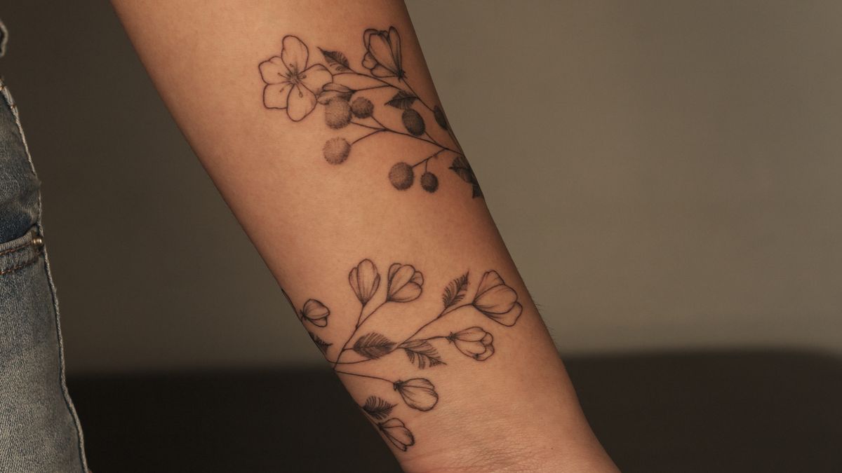 Two fine-line botanical flower branches tattooed along a forearm