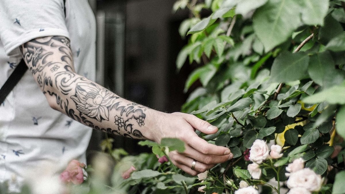 Man's forearm with a large Japanese-inspired peony flower tattoo and flowing black decorative lines