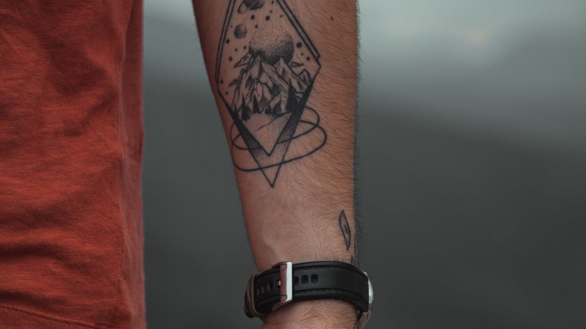 A geometric mountain design tattooed on a man's forearm with a fine-lined mountain ridge
