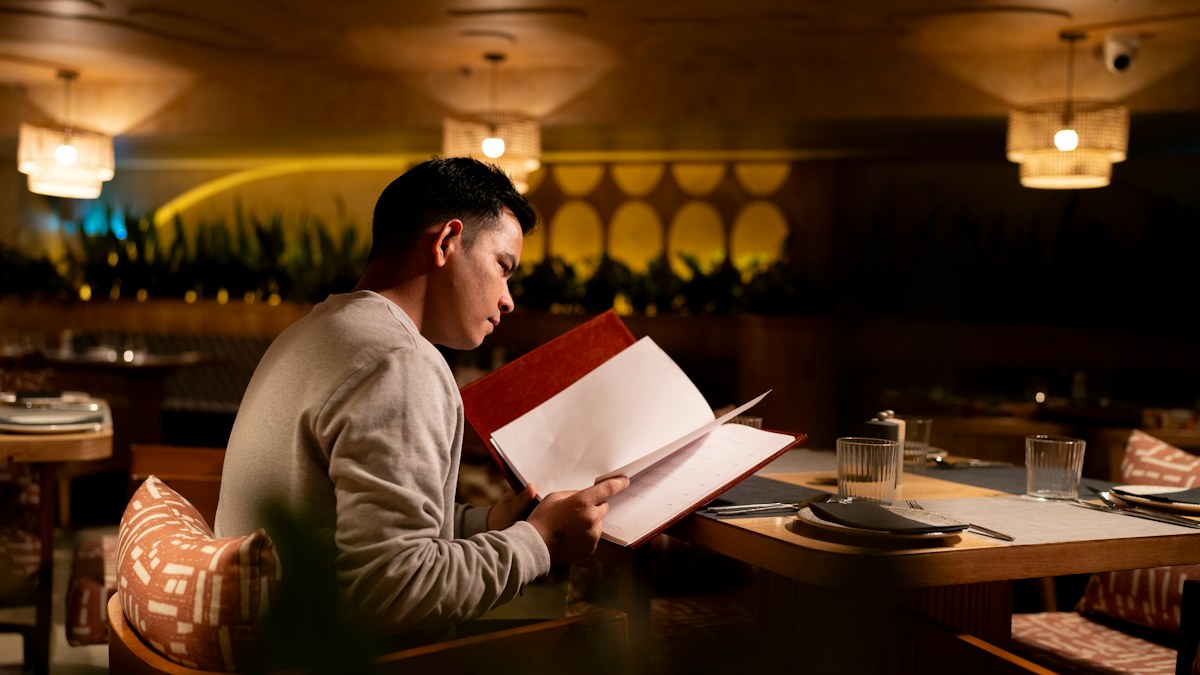 Man reading a restaurant menu at a warmly lit table