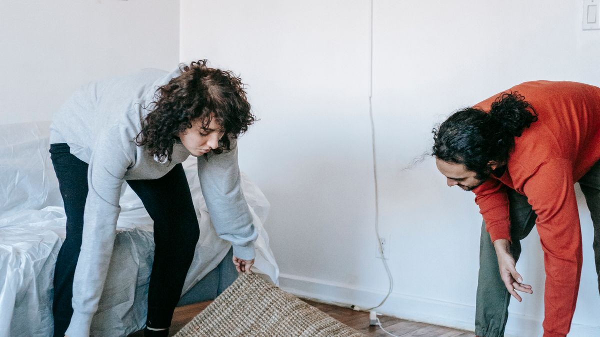 A couple lays out a large rug to define the room's usable seating zone