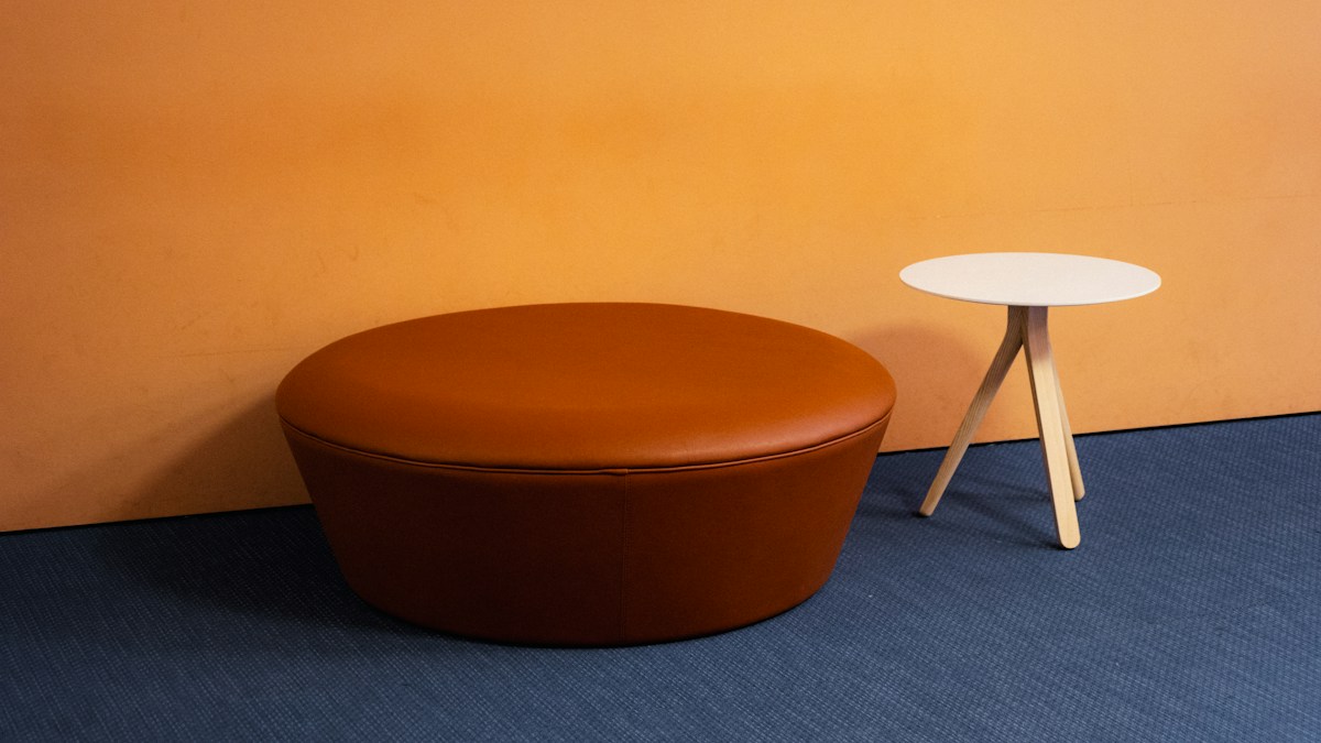 Brown ottoman with small side table against an orange wall