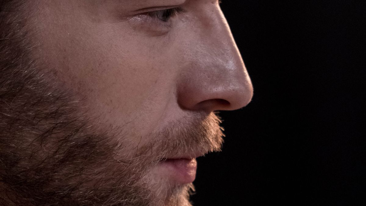 Close-up side profile of a man with a short beard and moustache against a dark background