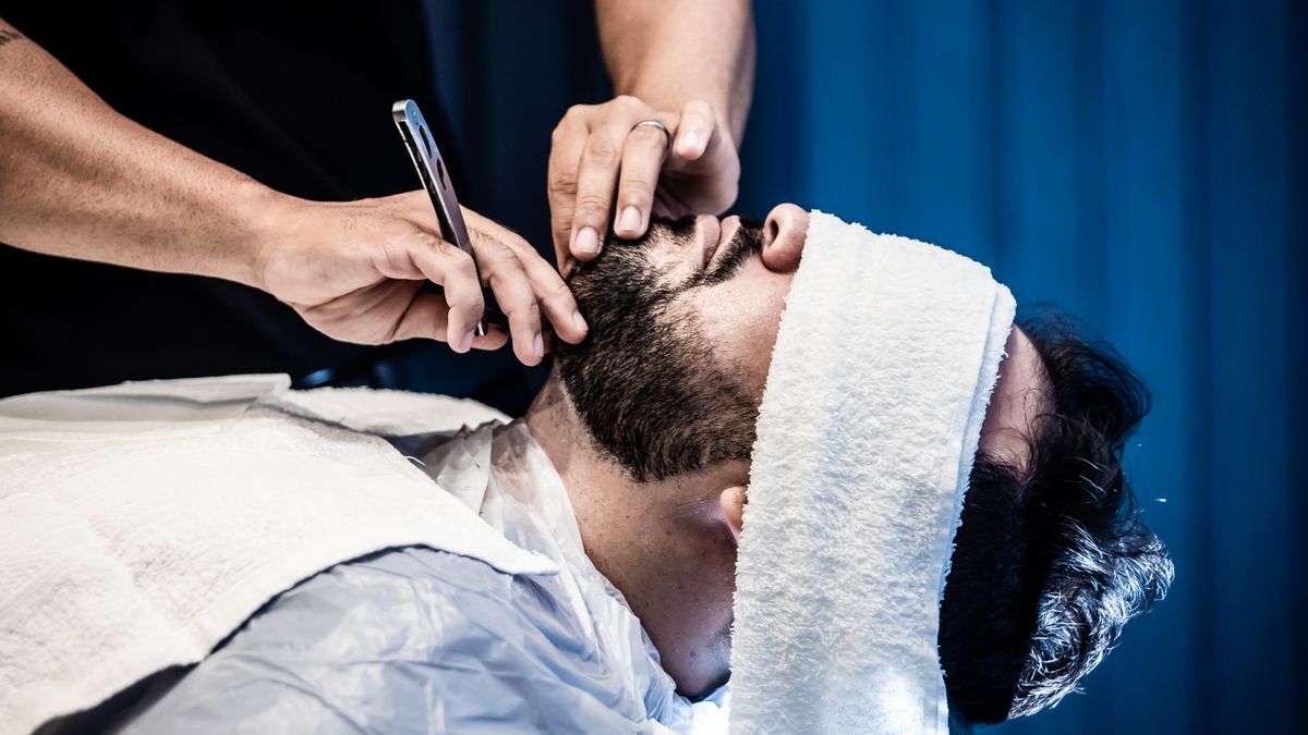 Barber carefully trimming a man's beard at a barbershop
