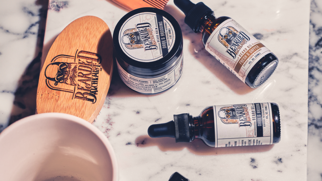 Flat lay of beard brush, wooden comb, beard oil and shaving tools on marble surface