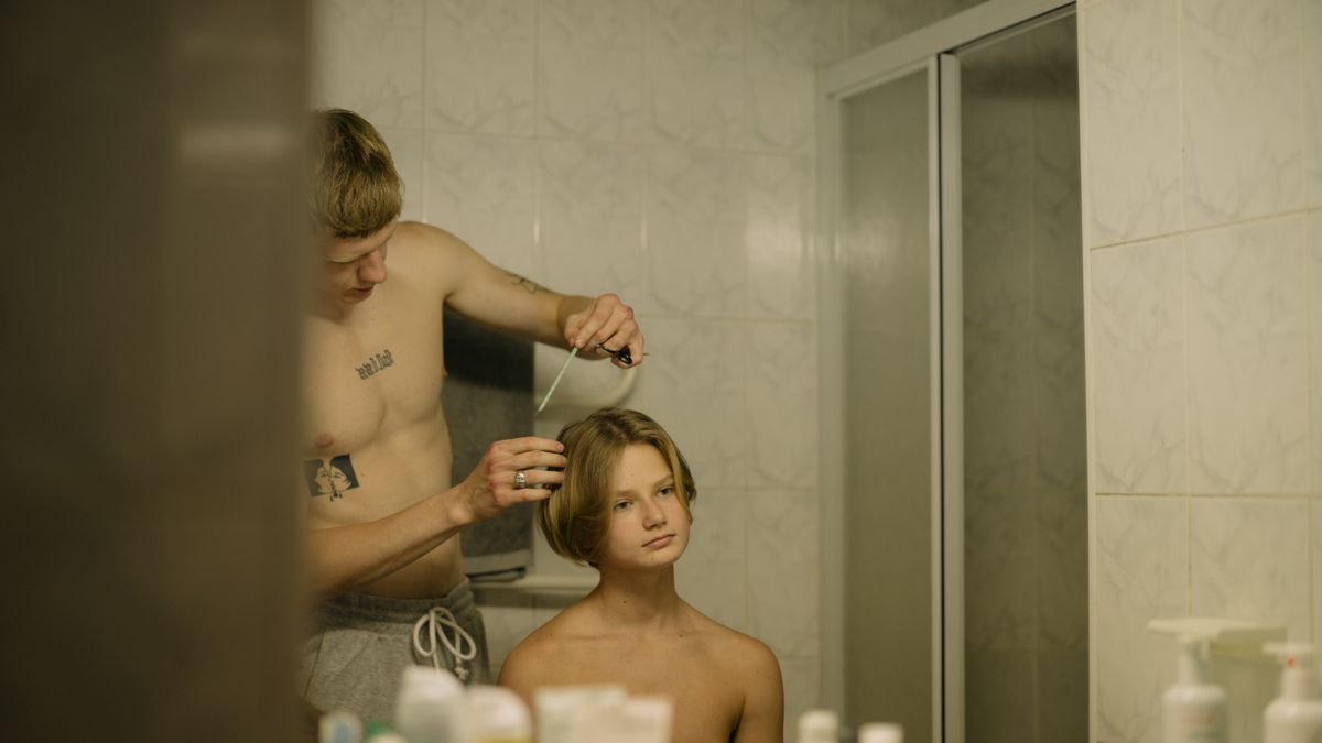 Hand holding a dark tub labeled fiber pomade