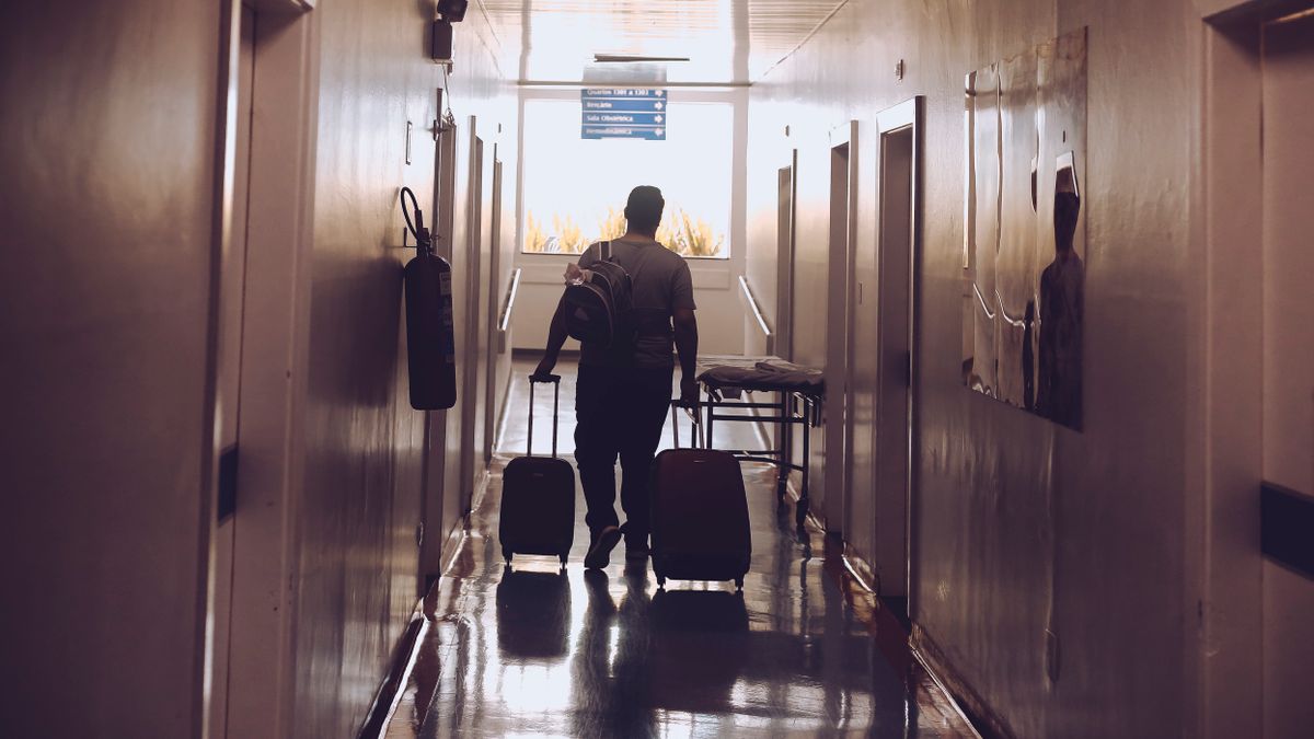 Man walking along an accommodation corridor pulling two wheeled suitcases.