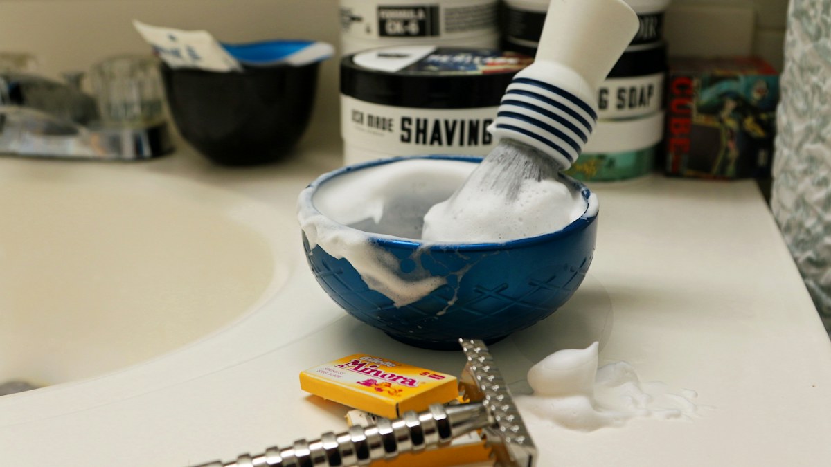 Shaving brush and lather in a blue bowl beside a safety razor