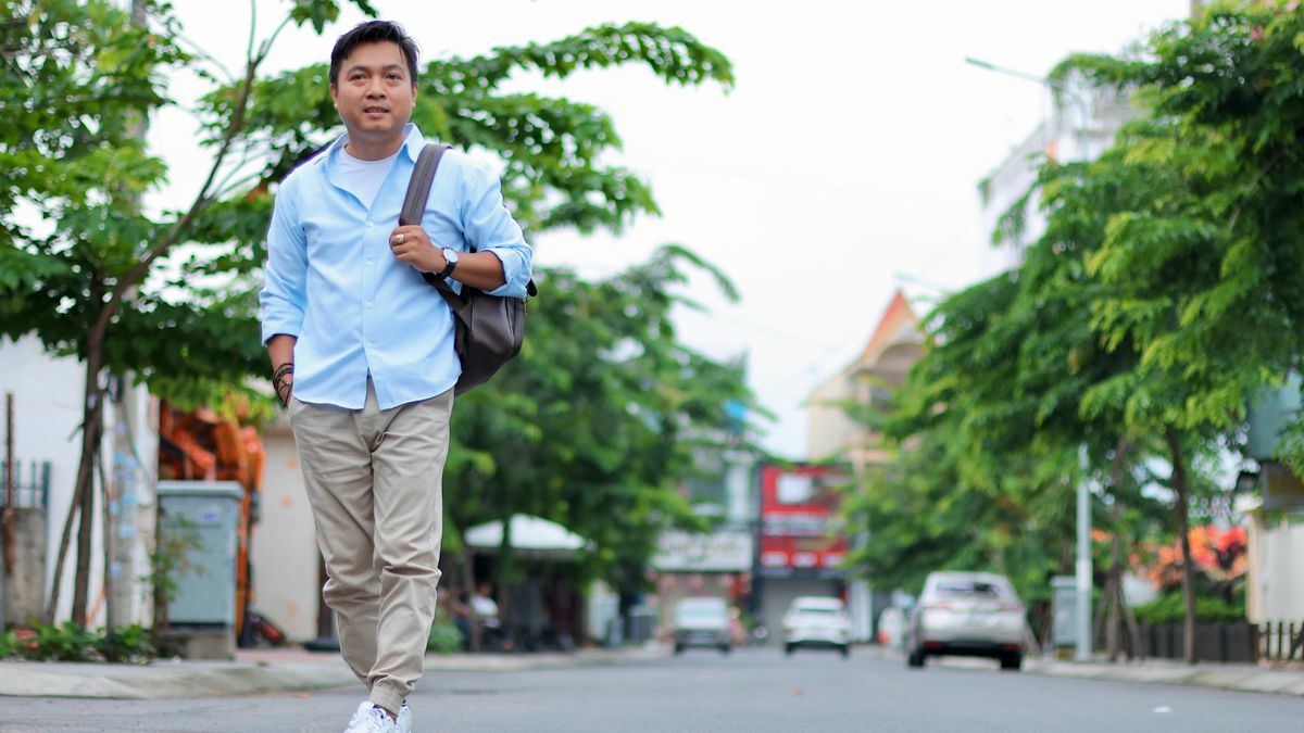 Man in blue shirt, khaki trousers and white sneakers walking on a sunny city street