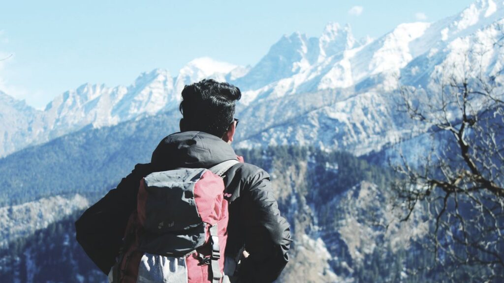 Man with backpack looking toward snowy mountains.