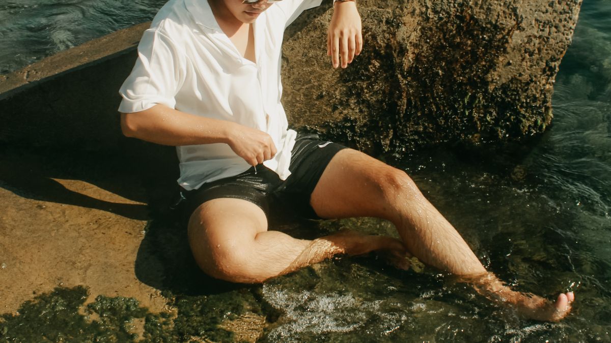 Man in a white polo shirt seated beside the sea.