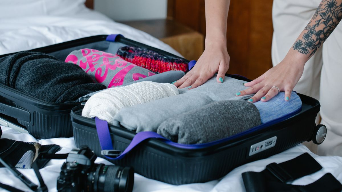 Hands placing rolled clothes into a suitcase.