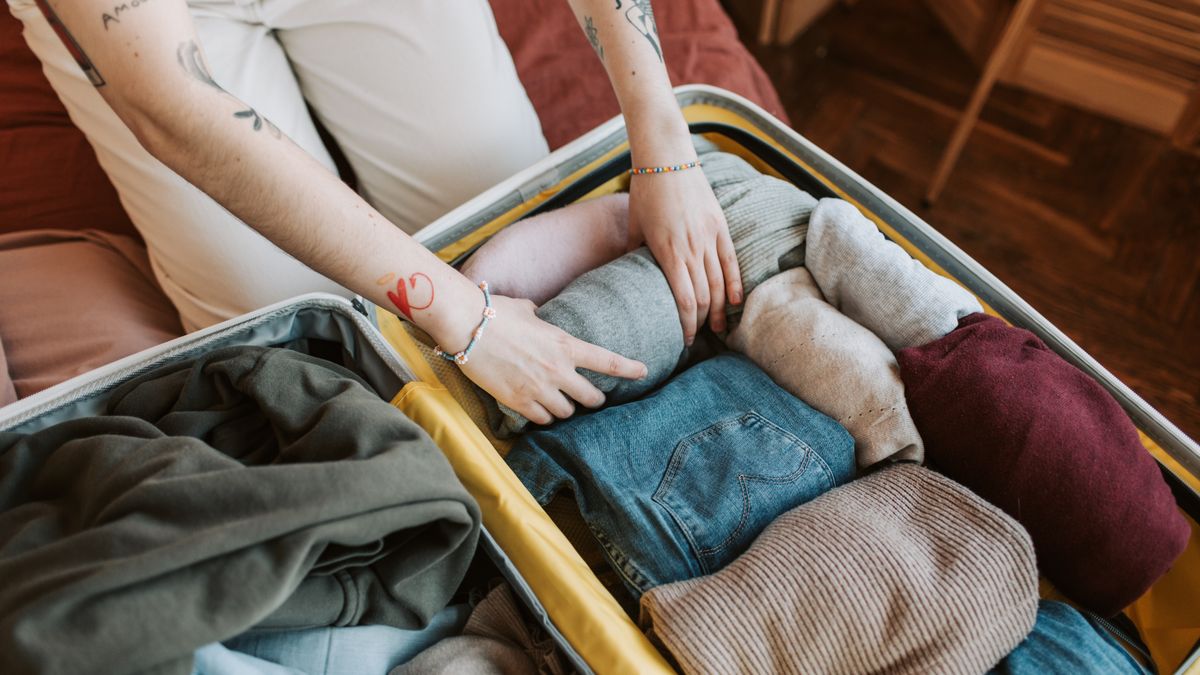 Hands organizing different clothes in an open suitcase.