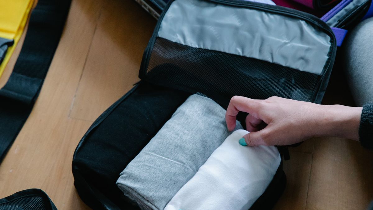 Hands packing folded clothes into a travel cube.