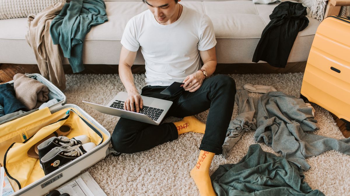 Man working on laptop beside an open suitcase.