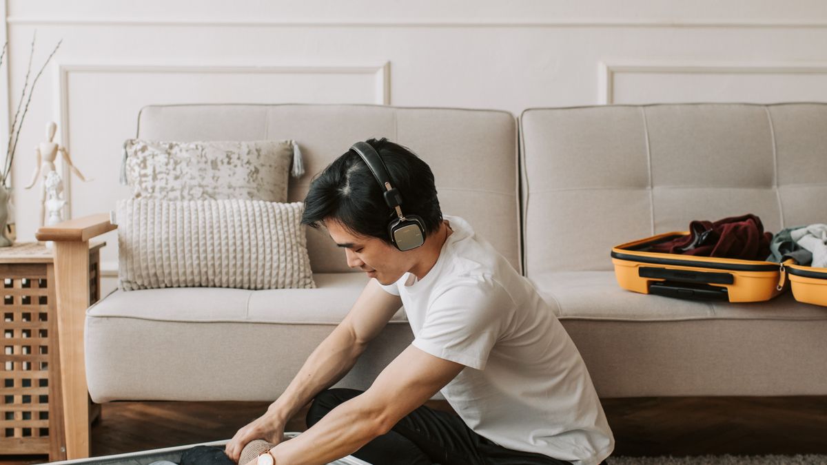Man packing travel clothes while wearing headphones.