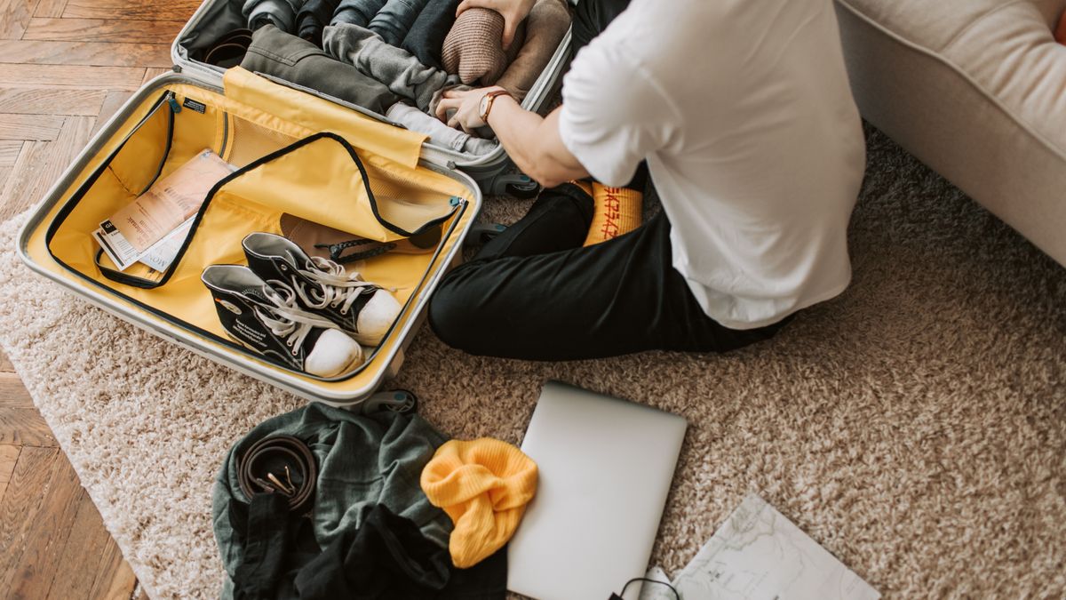 Man packing clothing and shoes into an open suitcase.