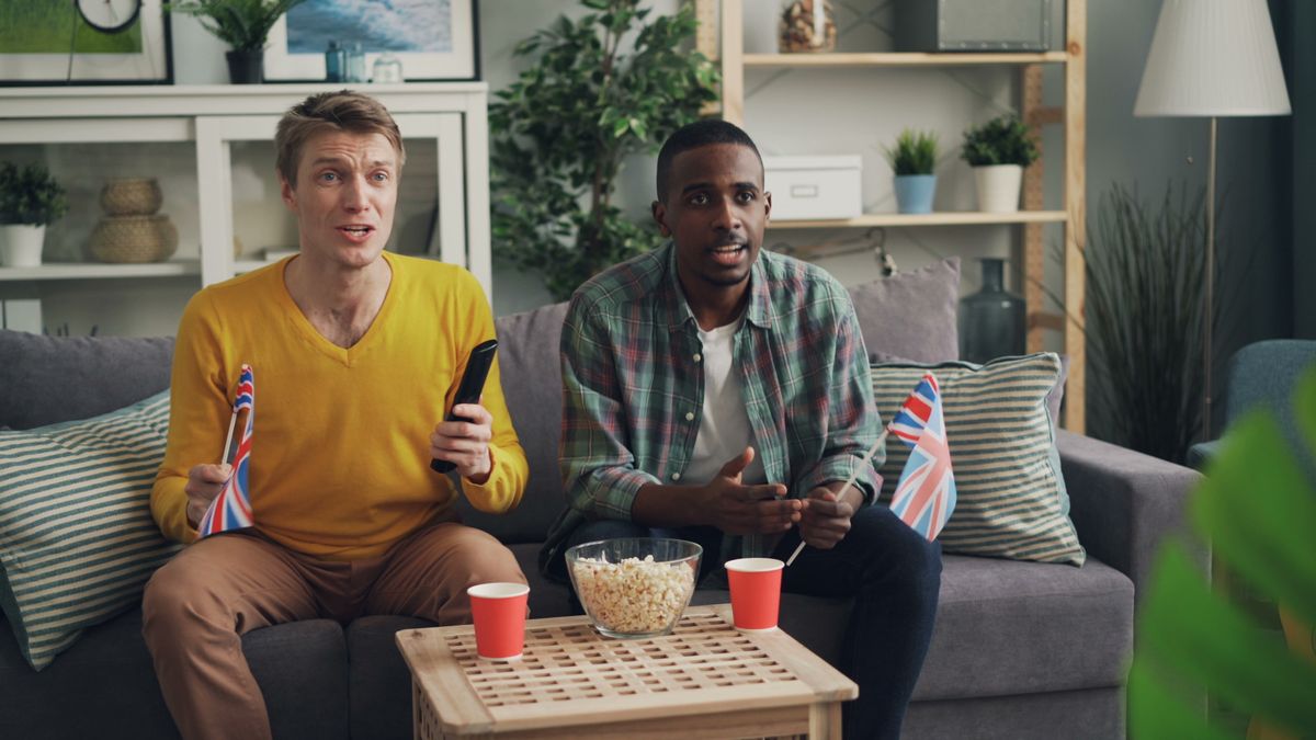 Two men share a sports-watching session on a living-room sofa