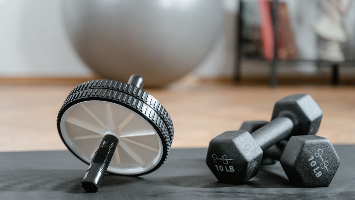 Compact workout tools, including dumbbells and an ab wheel, arranged on a mat