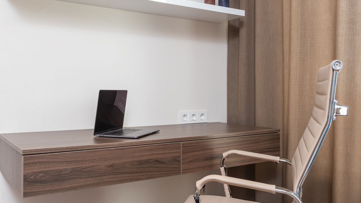 A compact desk with a laptop, chair and wall shelves illustrates a workstation that leaves the room flexible