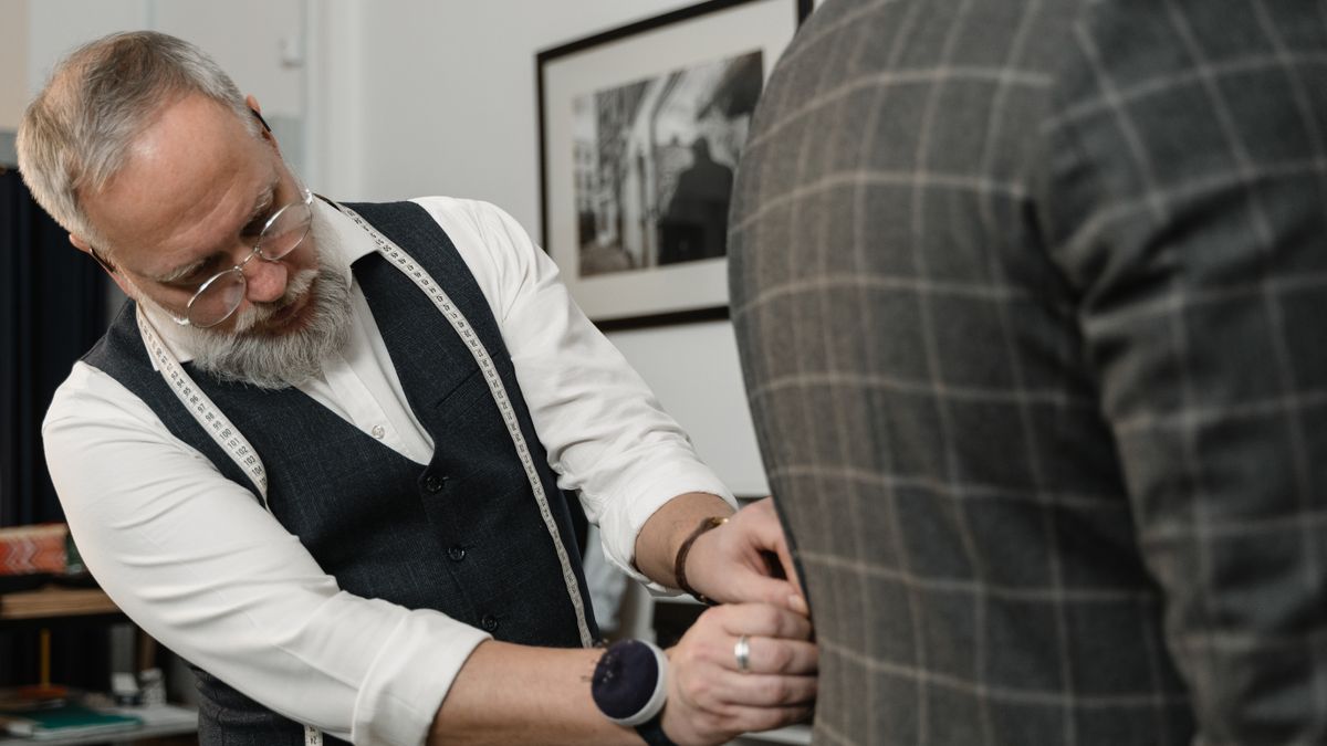 A tailor adjusting the fit of a man's checkered suit jacket