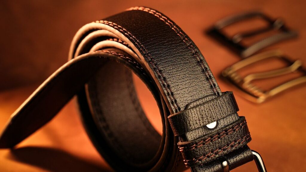 Brown leather belt threaded through jeans, showing strap width and buckle fit