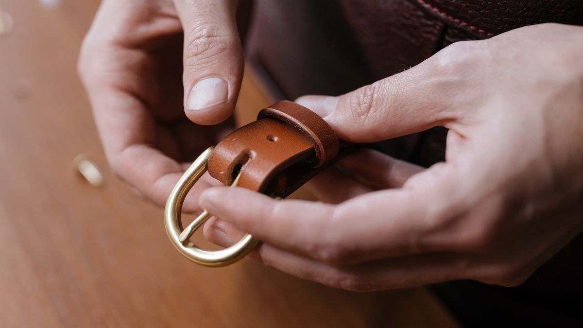 Hands examining a brown leather belt and metal buckle