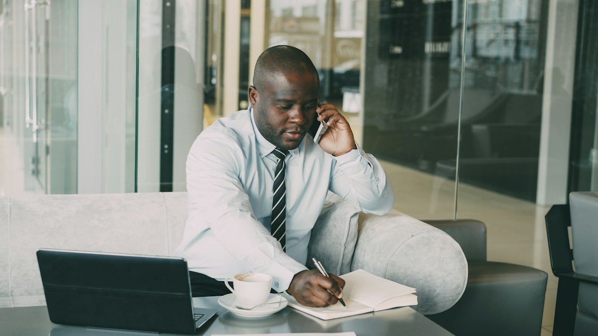 Man writing notes beside a laptop and coffee at a work table.