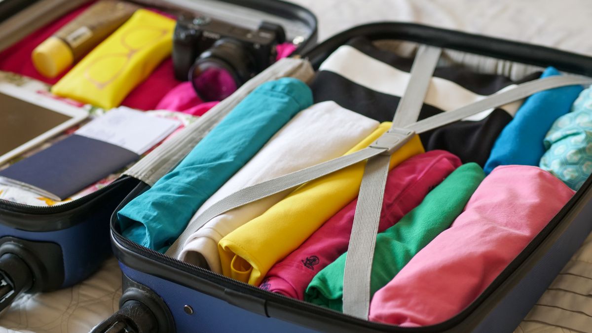 Open blue suitcase filled with folded colorful clothes and travel essentials.