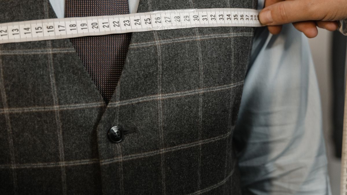 A tailor using a measuring tape across a man's suit vest