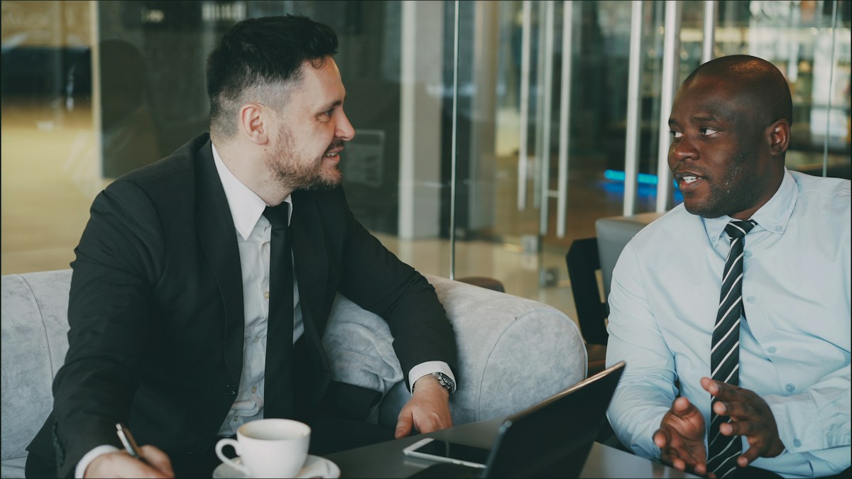 Two male colleagues reviewing notes and a laptop during a work discussion.